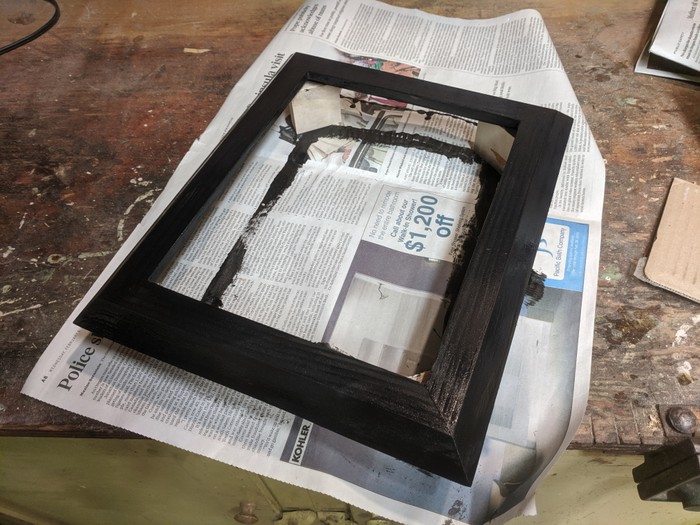 Rectangular frame painted black sitting on newspaper